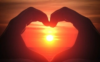 Mains formant un coeur sous le coucher du soleil.