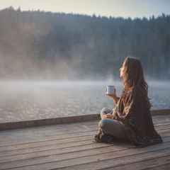 Femme buvant une boisson chaude sur un quai face au lac le matin.